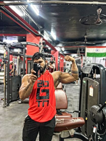A mirror selfie showing off the bicep pump. The red tank top makes the muscles pop.