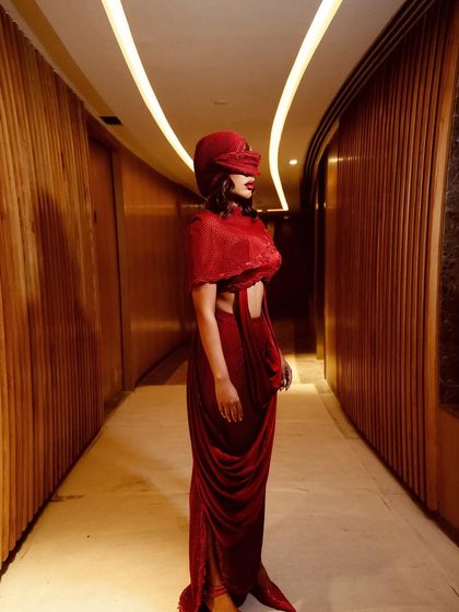 The crimson cowl-drape set seen from the side, highlighting its fluid lines and the mystery of its veiled headpiece.