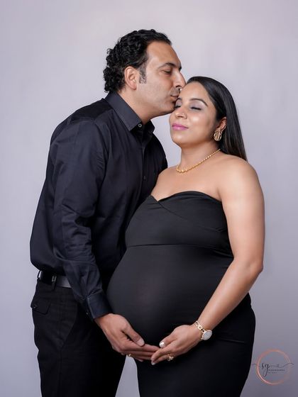 An elegant and intimate moment. The partner's gentle kiss on the forehead and hands on the bump create a portrait filled with love and tenderness.