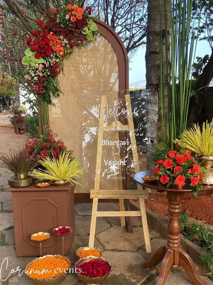 The welcome area for the backyard wedding, combining a modern acrylic sign with rustic rattan, wood, and vibrant flowers.