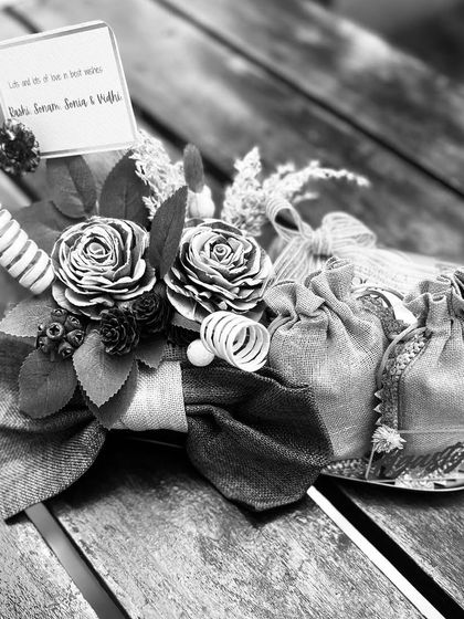 A black and white version of the gold coin platter, focusing on the rich textures of the burlap bow, wooden flowers, and delicate potli bags.
