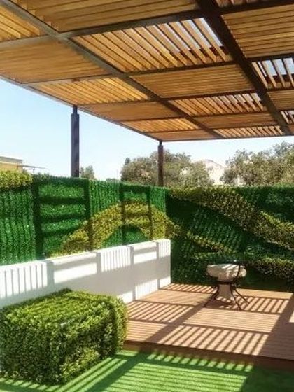 A creative use of artificial green walls on a terrace. This design combines a wooden slat pergola with a maintenance free vertical garden, creating a private and perpetually green space perfect for urban living.