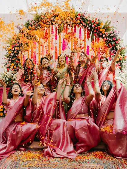 A joyous moment as the bride and her bridesmaids, all in matching pink sarees, throw flower petals in the air during the Haldi ceremony.