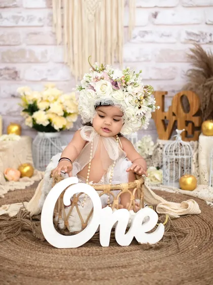 A beautiful and serene first birthday portrait. The elaborate floral bonnet and delicate details in this boho-chic setup create a truly artistic and memorable photograph to mark her first year.