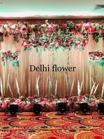 An elegant indoor reception stage with a backdrop of flowing drapes and delicate, artistic floral arrangements.
