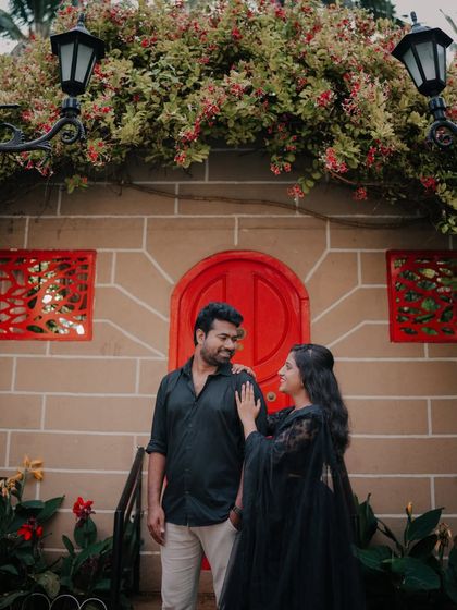 A romantic moment in front of a charming house facade with a bright red door and climbing flowers.