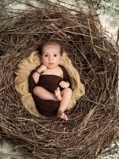 A curious newborn wrapped in a brown swaddle looks up from a rustic nest. This shot captures a beautiful moment of stillness and wonder.