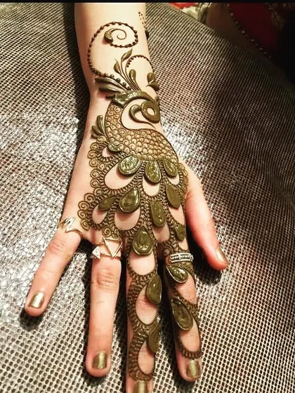 A unique and artistic take on the classic peacock mehndi. This design features a bold, 3D peacock whose feathers flow elegantly down the fingers, creating a striking and modern look that is sure to turn heads.