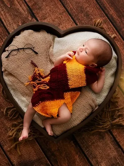 A creative newborn photoshoot with a Harry Potter theme, featuring a baby in a Gryffindor scarf lying in a heart-shaped prop. I enjoy bringing imaginative ideas to life for a truly unique portrait.