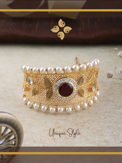 Embrace the elegance of this Gold Kada. The intricate filigree work is complemented by a central red stone and a border of pearls, creating a unique and stylish piece.