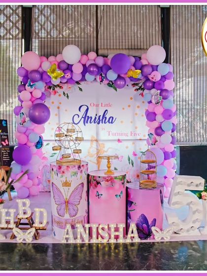 A full-stage butterfly-themed fifth birthday. The purple and pink decor features a 'Our Little Anisha' backdrop, large butterfly cutouts, and a 'ANISHA' marquee.