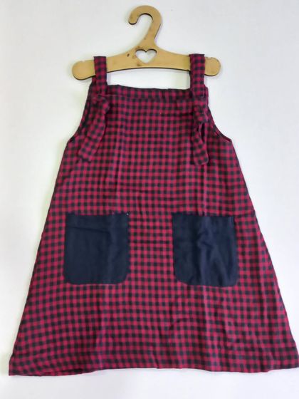 A classic knot dress in a red and black check pattern. You can just tie the knots on the shoulders and your little one is ready to go. It can be worn on its own or with a t-shirt underneath for cooler days.