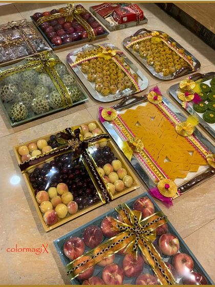 An assortment of wedding trays filled with fresh fruits and traditional Indian sweets, beautifully wrapped and ready for gifting during wedding ceremonies.