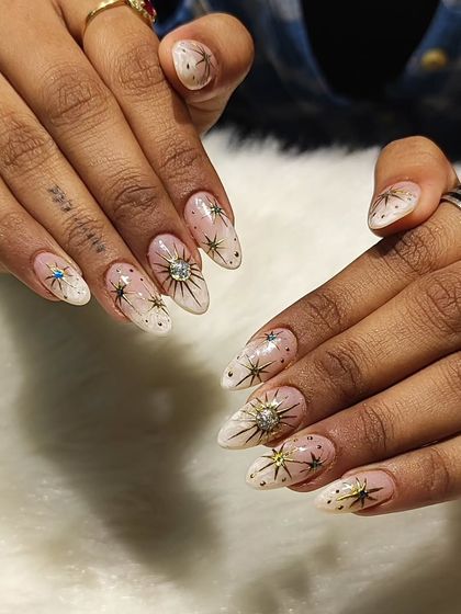 If the universe had fingertips, they'd look like this. This is another celestial-themed transformation, featuring a white ombre base with intricate, hand-painted gold and rhinestone starbursts.