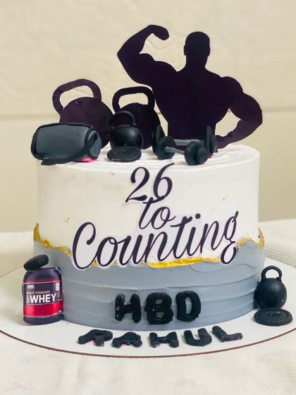 A detailed gym-themed cake with protein powder tubs and weights.