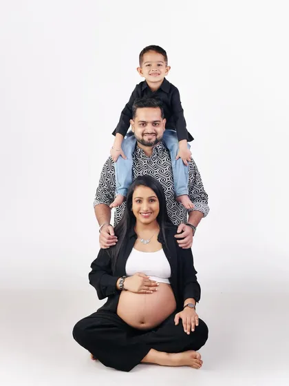 A creative family pose, with the son sitting on his father's shoulders, forming a tower of love above the expecting mother.