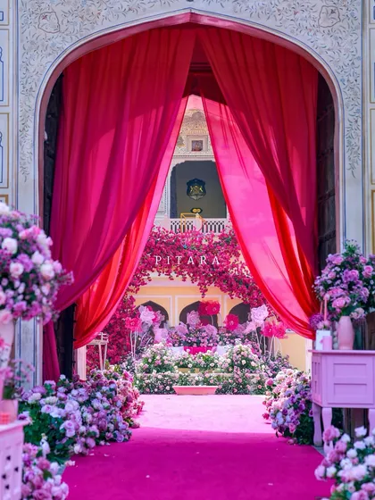 This is how we do royal entrances. A vibrant gulabi carpet and lush floral arrangements guide guests through majestic palace arches, framed by dramatic fuchsia drapes. It’s a welcome that promises the grandeur to come.