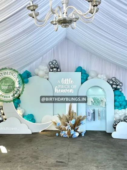 A "Little Piece of Heaven" baby shower with a celestial theme. The setup, under a white tent, features moon and cloud cutouts and a beautiful teal, silver, and white color scheme.