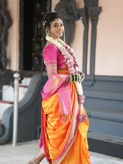 A full shot of the bride in her vibrant orange and pink Nauvari saree, draped perfectly for her wedding day.