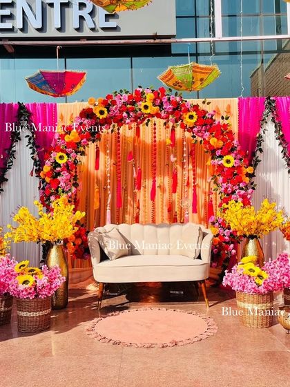 An outdoor Mehendi setup bursting with color. This design features a floral arch, colorful drapes, and traditional umbrellas, creating a carnival-like atmosphere.