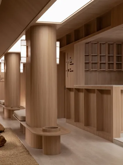 The waiting lounge, where curved wooden pillars and integrated benches create a soft, organic rhythm. The space is a meditative pause, designed for comfort and tranquility.