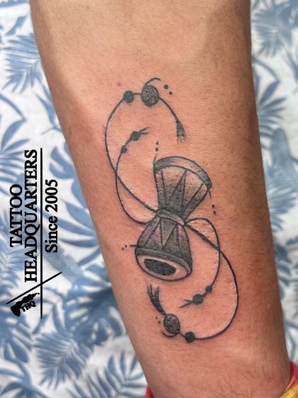 A tattoo of a Damaru, Lord Shiva's drum, with decorative strings, symbolizing the rhythm of creation and the cosmic heartbeat.