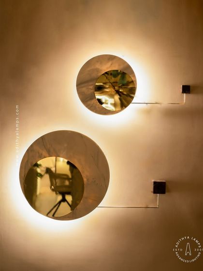 A modern wall sconce featuring a disc of white marble with a gold-mirrored circular cutout. The backlight provides a soft, ambient halo, making it a sophisticated and elegant choice for hallways or flanking a master bed.