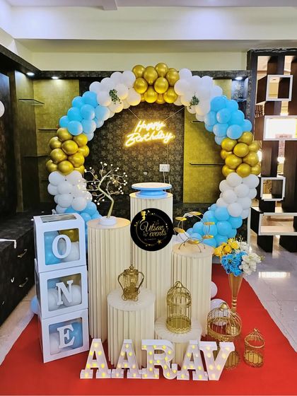 A blue, white, and gold ring-themed decoration for a first birthday. The setup includes 'ONE' blocks and a neon sign for a modern and celebratory look.