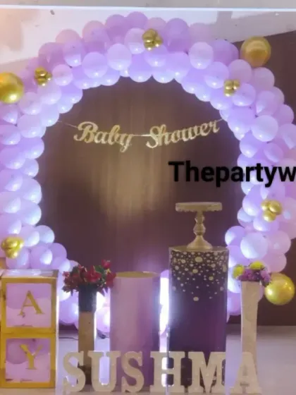 A pretty baby shower setup with a lavender and gold balloon arch. The "BABY" blocks and light-up name sign add a personalized and glamorous touch.