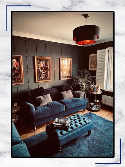 A living room designed for comfort and style. The deep blue velvet sofa and ottoman create a bold focal point, complemented by dark wall paneling and curated art.