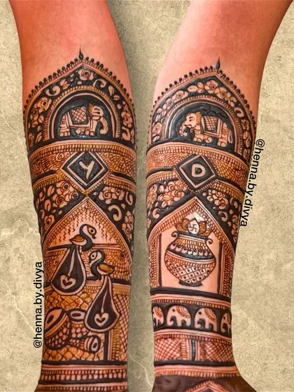 Another detailed shot of a bridal forearm design. This piece includes the couple's initials, a kalash, and birds carrying auspicious symbols, all rendered in a bold, clean style.
