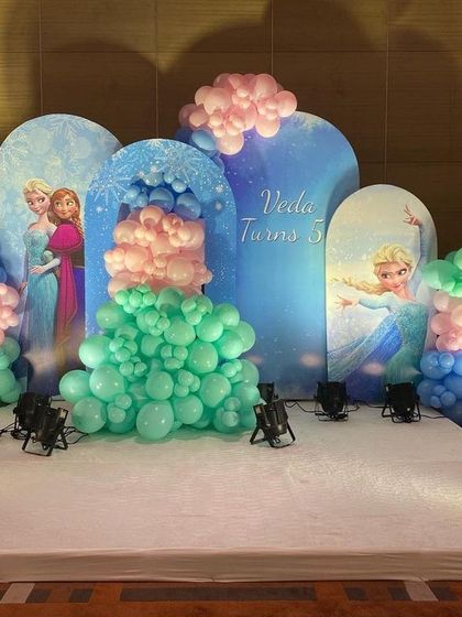 A grand stage setup for a Frozen-themed party. This decoration uses multiple arched backdrops with characters and a pastel balloon arrangement to create a magical winter scene.