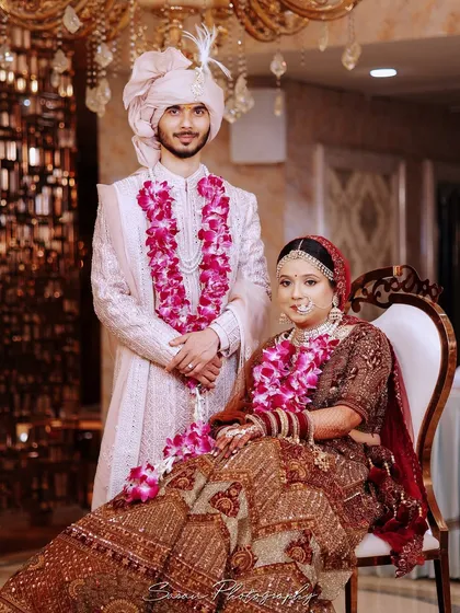 A regal portrait of the wedding couple, with the bride seated and the groom standing beside her.
