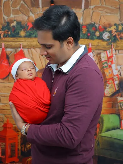 A father's gentle hold. This portrait shows a dad gazing lovingly at his newborn, who is wrapped in red and wearing a Santa hat, capturing a tender moment during a Christmas-themed shoot.