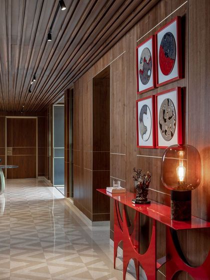 A long corridor lined with wood panels and accented by a vibrant red console table. We use art and statement furniture to turn transitional spaces like hallways into memorable design moments.