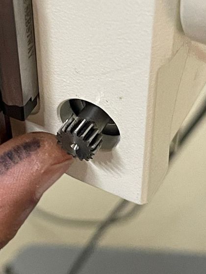 A finger points to the small but crucial gear that was repaired. This image highlights the precision and attention to detail required in advanced repair work.