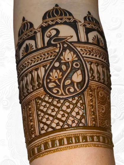 A detailed close-up of an arm band for an engagement, featuring a peacock with its tail filled with lotus flowers, set against a palace-like backdrop.