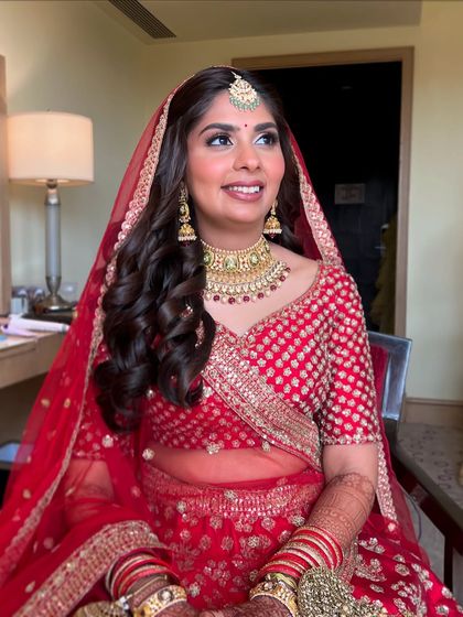 The joy on her face says it all. For her wedding day, we went with a classic look featuring soft curls, glowing skin, and a beautiful red lehenga.