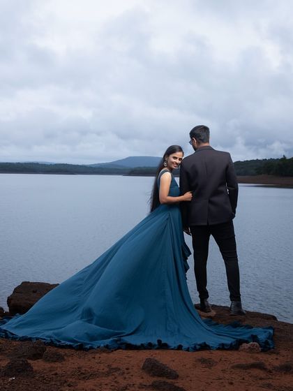 A serene and romantic pre-wedding photo overlooking a lake. The long trail of the blue gown adds a touch of elegance to the natural scenery.