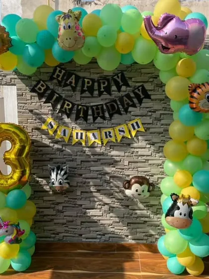 A full view of the jungle-themed balloon arch for a third birthday. We use a mix of green and yellow balloons with cute animal faces to create a fun and inviting party entrance.