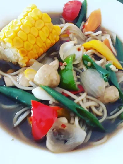 A comforting Chinese-inspired bowl filled with soupy noodles, corn on the cob, and a medley of crunchy vegetables in a savory garlic sauce. It's a one-bowl wonder for a chilly evening.