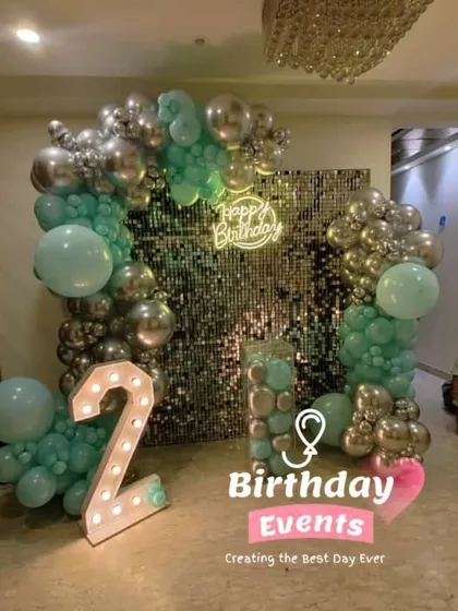 We love creating modern and stylish birthday themes, like this one for a second birthday. The setup features a trendy silver shimmer wall, a 'Happy Birthday' neon sign, and a balloon arch in a fresh mint green and silver color scheme.