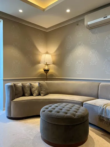 A curved sofa is perfect for creating a cozy and intimate corner. Here, we paired it with a tufted ottoman and subtle damask-patterned wallpaper to design a comfortable and stylish nook for relaxation.