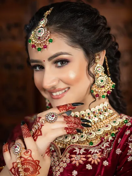 A perfect example of a soft and radiant bridal look. The focus here is on luminous skin and a warm, smiling expression, complemented by a classic red velvet lehenga and traditional jewelry.