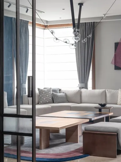 This view through a fluted glass partition shows the layered design of the living room. The soft gray sofa and modern lighting fixture create a comfortable yet stylish space for relaxation.