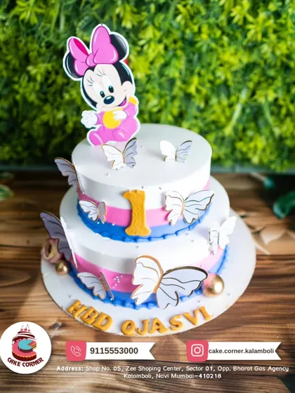 A two-tier Minnie Mouse cake with beautiful butterfly decorations. The pink, blue, and white colours create a soft and magical look for a first birthday.