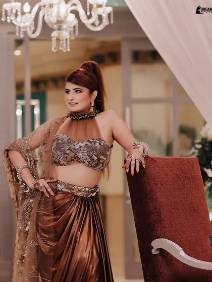 Kirti posing elegantly by a chair, her halter-neck blouse and high ponytail creating a very chic look.