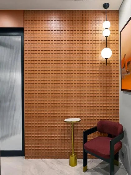 This waiting area uses a warm, terracotta-colored tile wall to create a welcoming and textured feature. The simple, elegant furniture complements the bold wall, creating a balanced and inviting corner.