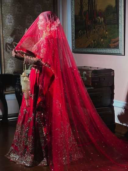 A dramatic and beautiful shot of the bride under her red veil. This photo captures the grandeur and tradition of an Indian wedding.