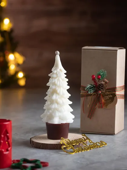A beautiful white Christmas tree candle, displayed on a wooden slice next to its gift box. It's a simple, elegant gift.